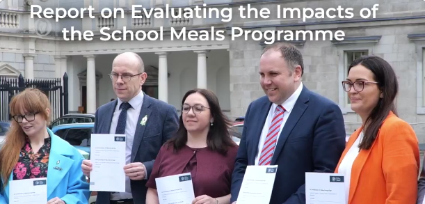 Four people holding a document, the report evaluating the impacts of the school meals programme, in front of the Oireachtas in Ireland.